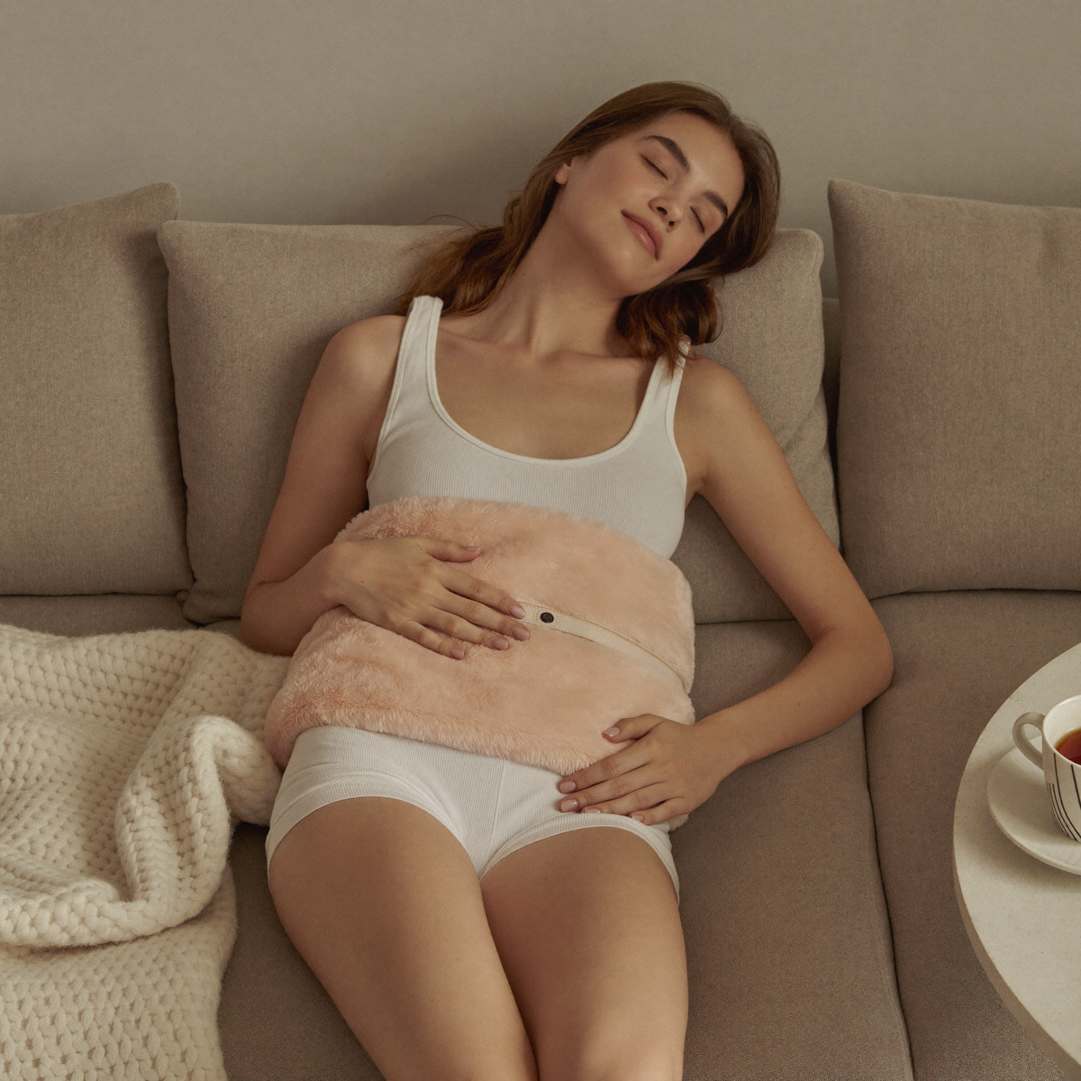 Femme détendue sur canapé portant la ceinture chauffante LUNARA sur le bas du ventre
